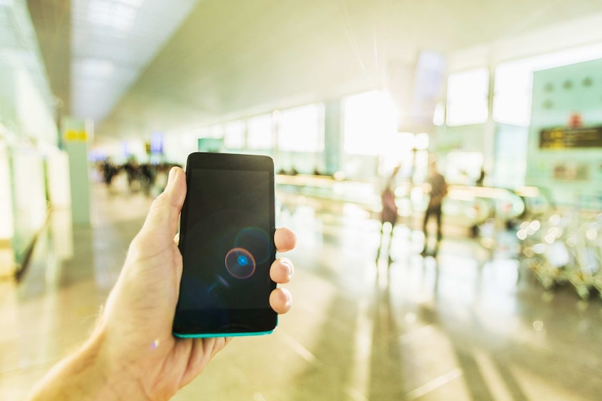 A male hand holding a smartphone in an airport terminal.