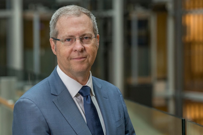 A man in a grey suit looks at the camera