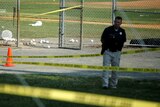 A police officer mans a shooting scene near a baseball field.