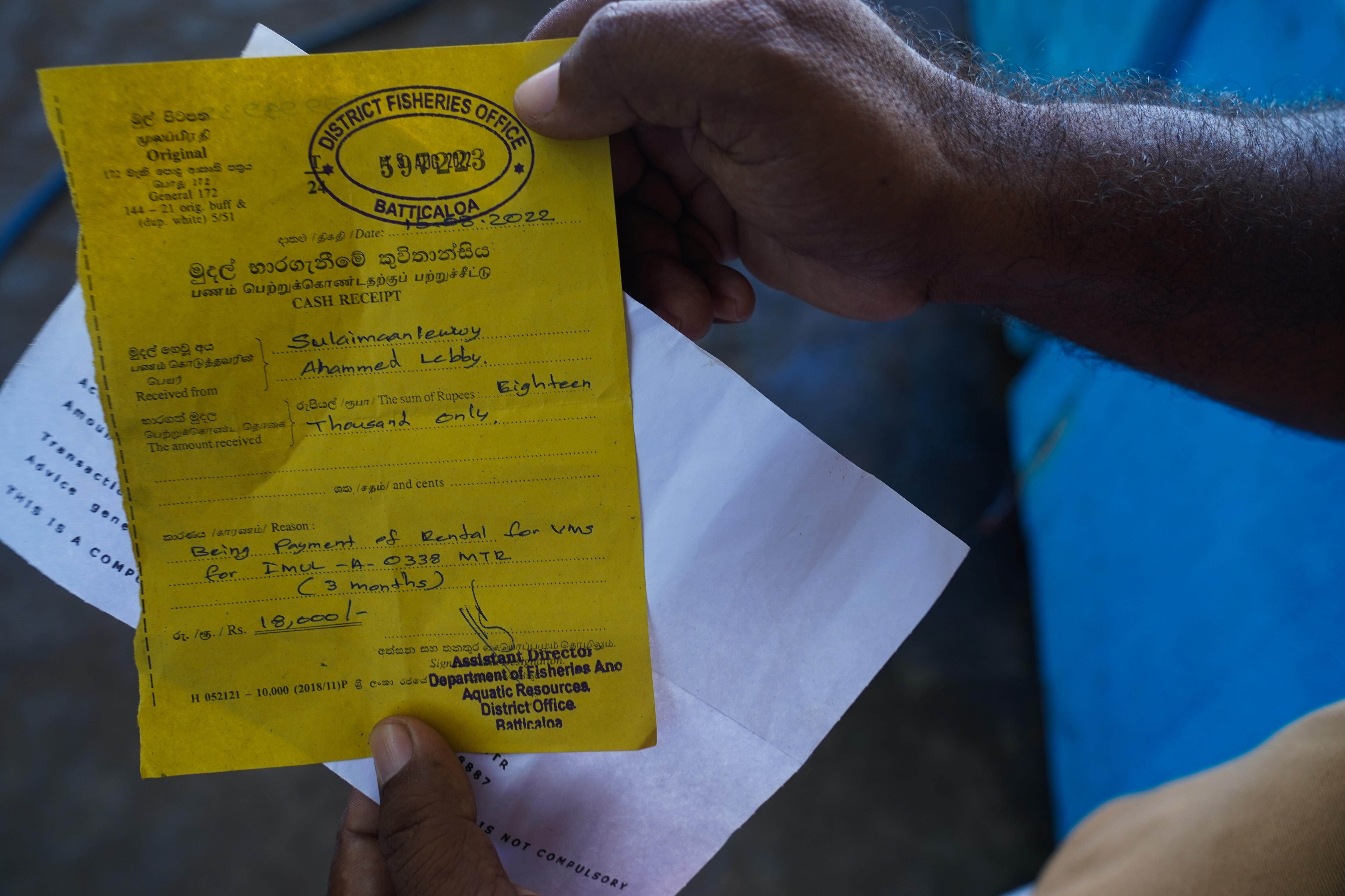Two hands hold out a yellow piece of paper with a stamp bearing the words DISTRICT FISHERIES OFFICE
