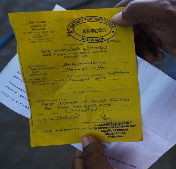 Two hands hold out a yellow piece of paper with a stamp bearing the words DISTRICT FISHERIES OFFICE