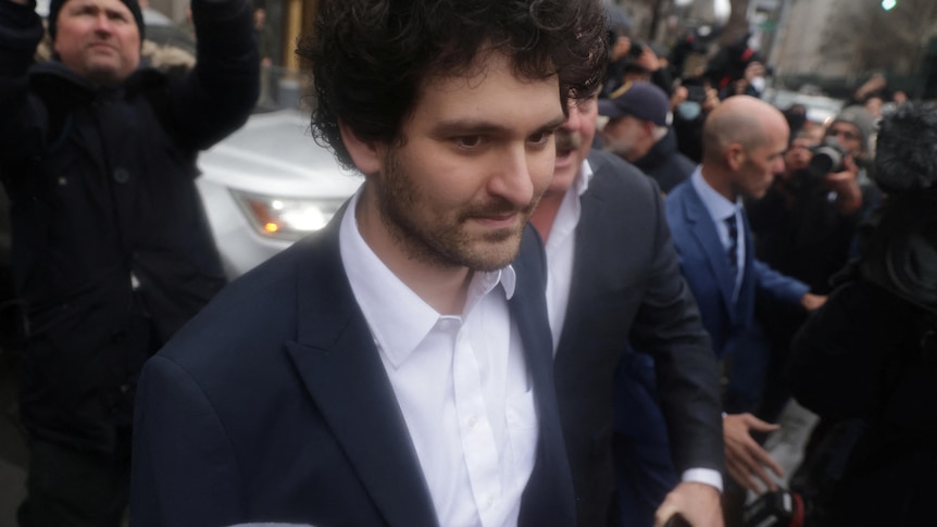 A man in a grey and white suit surrounded by photographers