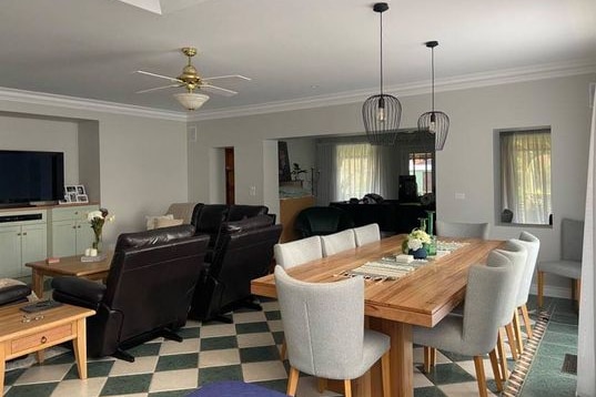 A grey living room with white features is seen with a dining table and sofas in front of a TV. 