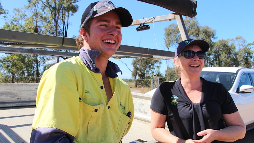 A young man in a yellow high-vis shirt and a woman leaning against a ute tray, smiling.