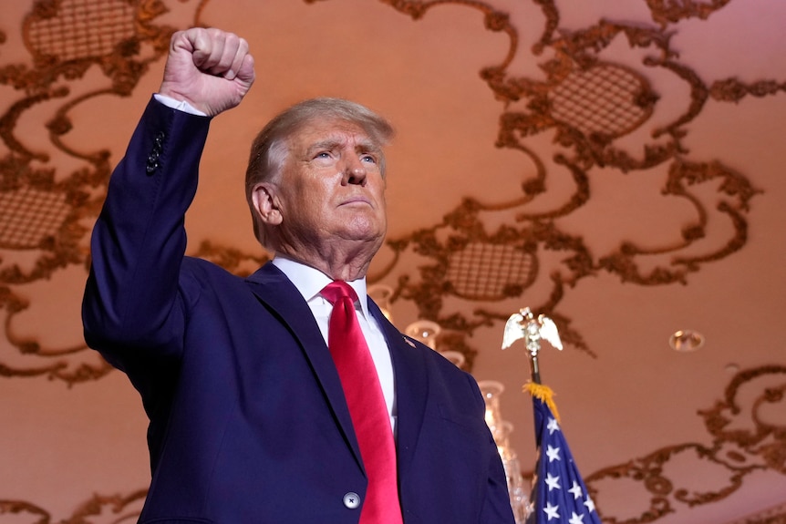 Donald Trump, wearing a suit and tie, stands and raises his clenched fist into the air
