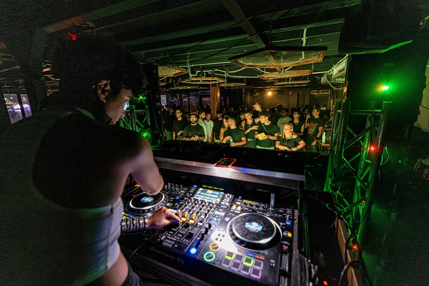 a woman DJs at a DJ console inside a club in Cairo, with many people on the dancefloor in front