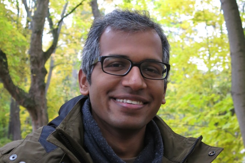 A middle-aged man, smiling in a forest.