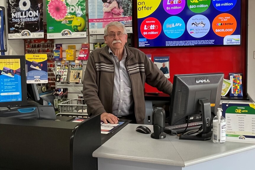A man standing at the front desk in the newsagency.