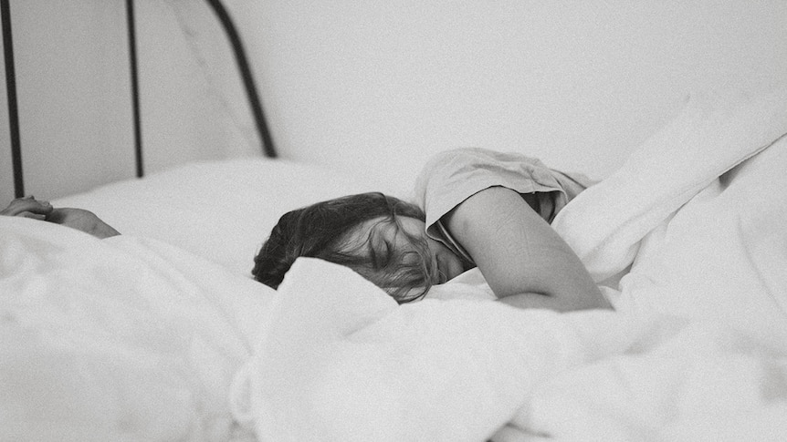 A black and white photo of a woman sleeping in a bed