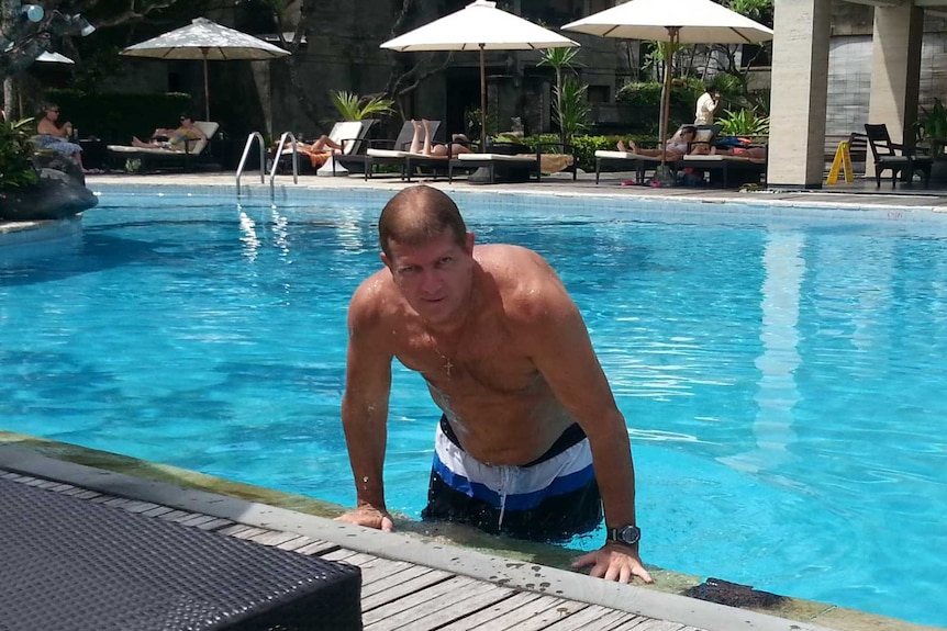 A man lifts himself out of a pool in a tropical resort.
