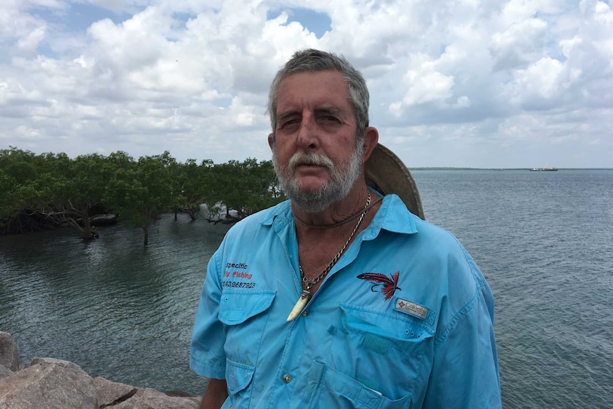 A man stands by mangroves at the water's edge.