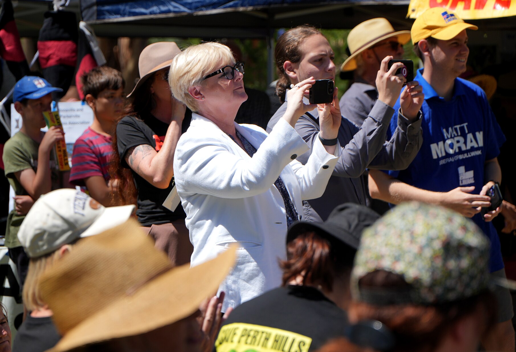 Linda Reynolds in a white blazer, taking a photo with a phone