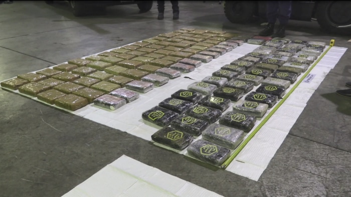 Brown and black packages full of cocaine laid out in rows on a white mat on a concrete floor.