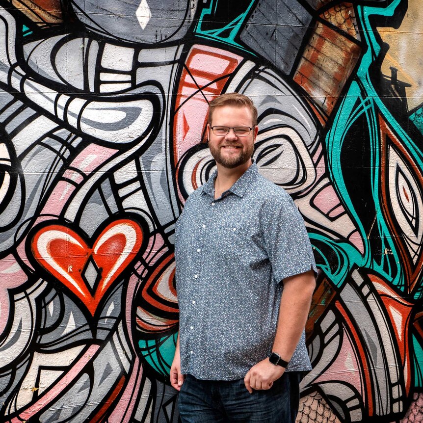 Ross Kay standing in front of a street art mural painted on a brick wall.