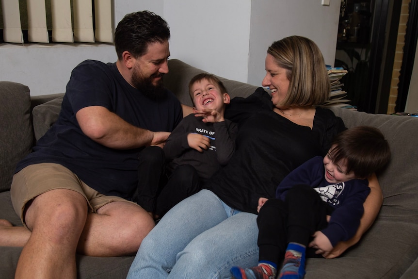 Young family sits on couch, laughing together.