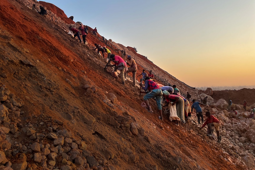 People climb a mine embankment at dawn.