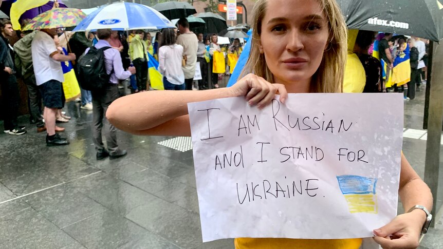 A woman holds up a sign saying she is Russian but stands in support of Ukraine. 