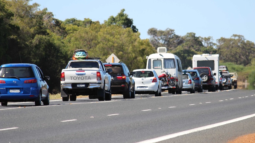 A range of cars and caravans lined up in traffic along a regional one lane highway