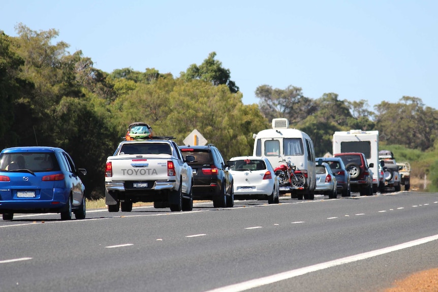 A range of cars and caravans lined up in traffic along a regional one lane highway