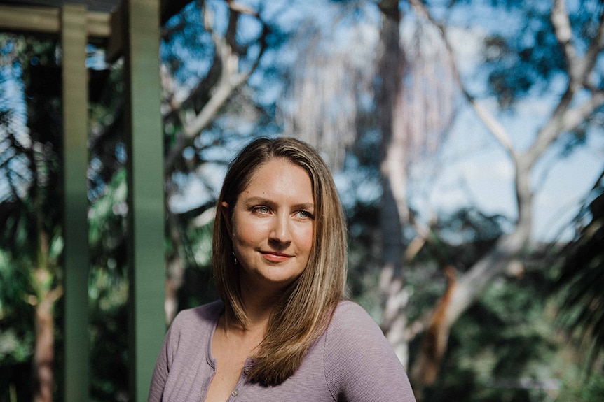 Colour photo of Joanna Erskine standing on sunny balcony to the backdrop of trees.