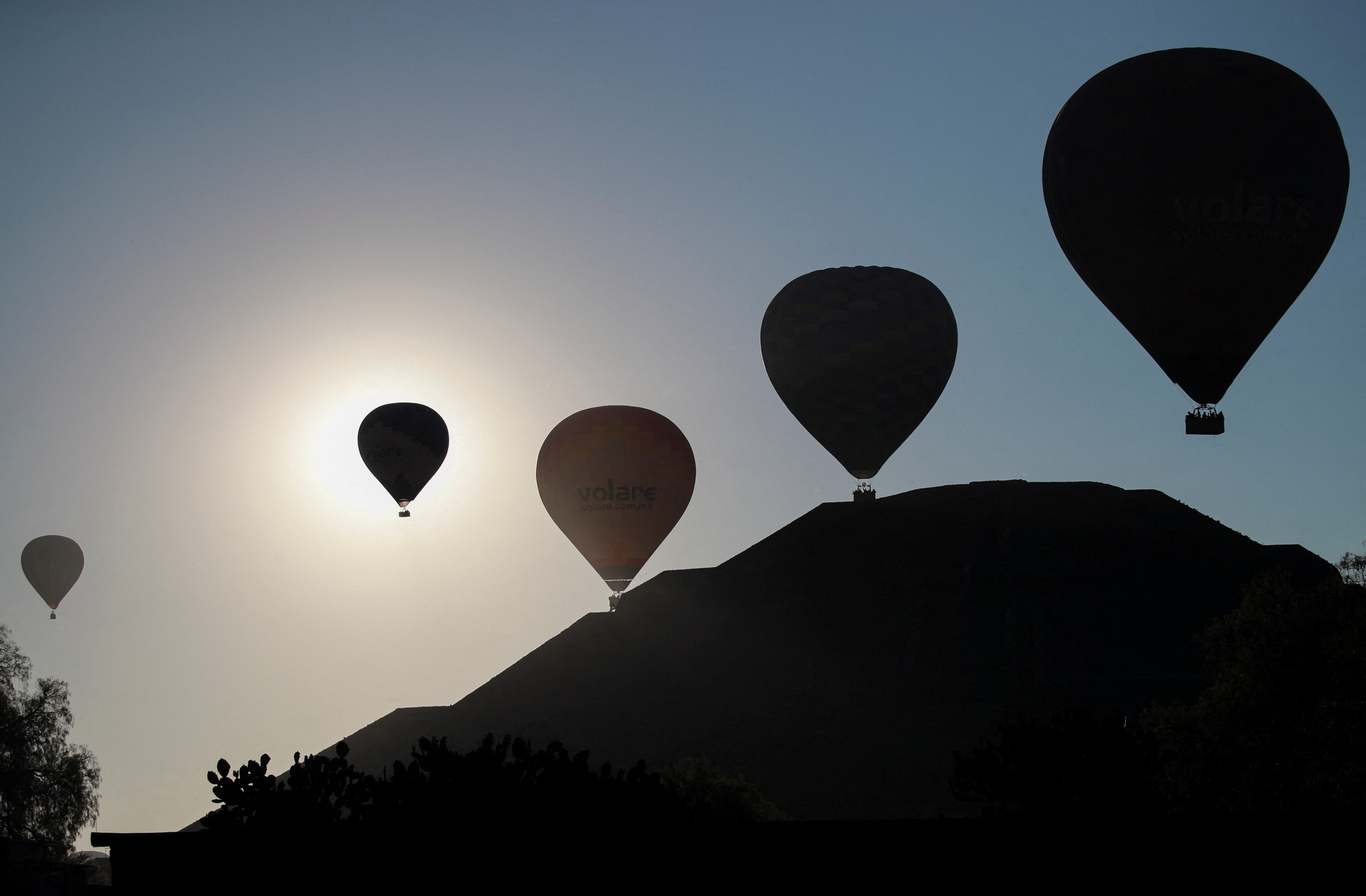 Silhouettes of hot air balloons above a large, stepped pyramid.