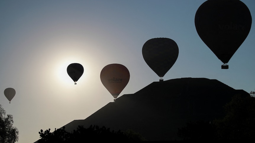 Silhouettes of hot air balloons above a large, stepped pyramid.