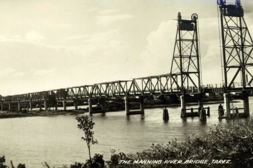 A black and white photo of a bridge over a river, with the drawbridge in the middle raised.