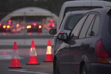 Cars lined up in the evening alongside traffic cones.