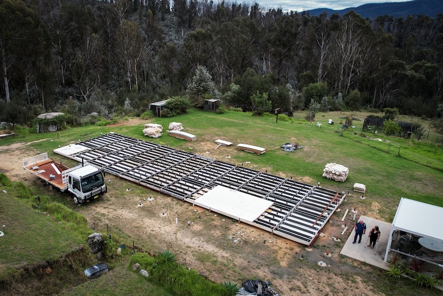 aerial image of a couple walking beside house foundations, surrounded by burnt trees