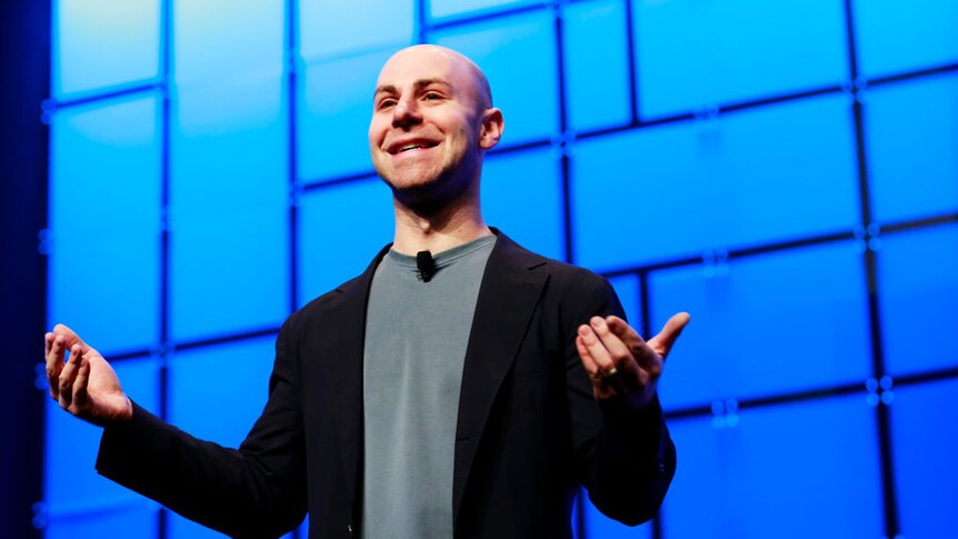 Adam Grant standing in front of a blue screen with open arms