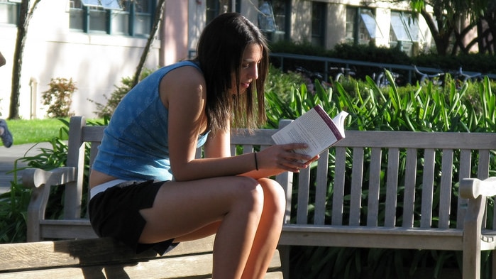 A woman sits on top of a bench reading