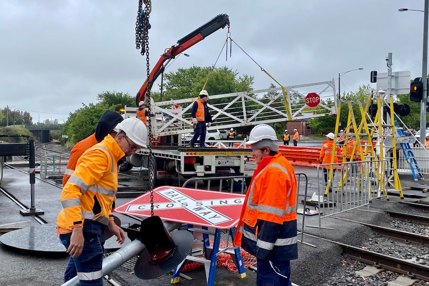Construction workers use a crane to lift an wooden railway crossing gate onto a truck.