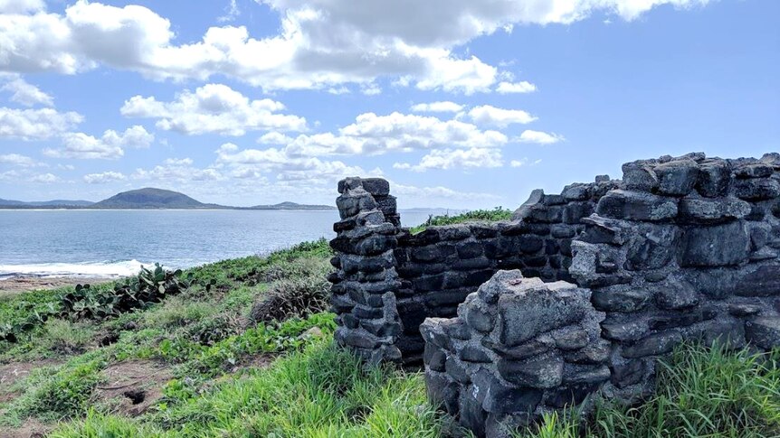 A cobblestone structure with no roof at the top of an island, overlooking the mainland.