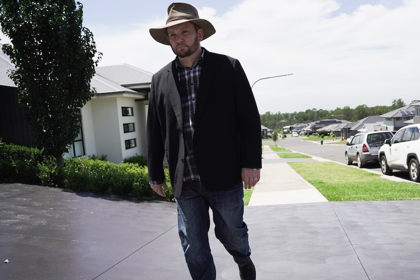 A man in a long coat and hat walks through a residential area.
