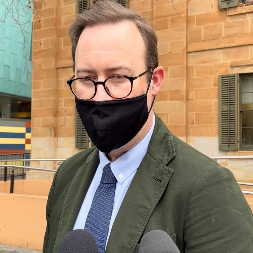 A man wearing a black face mask outside a sandstone building