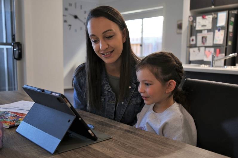 A woman and child looking at a laptop on a dining table.