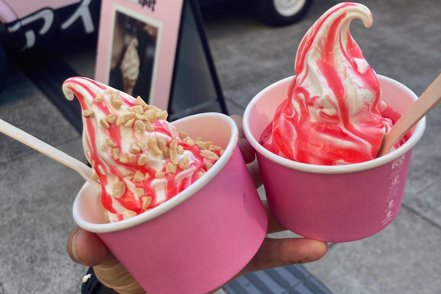 Two cups of soft serve ice cream with strawberry syrup drizzled on top.