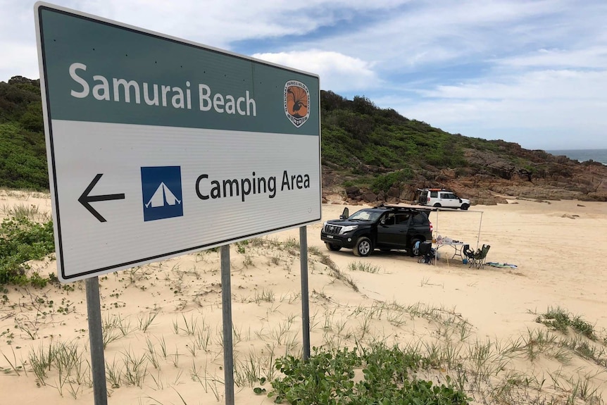 sign on beach with camping site in background on sand