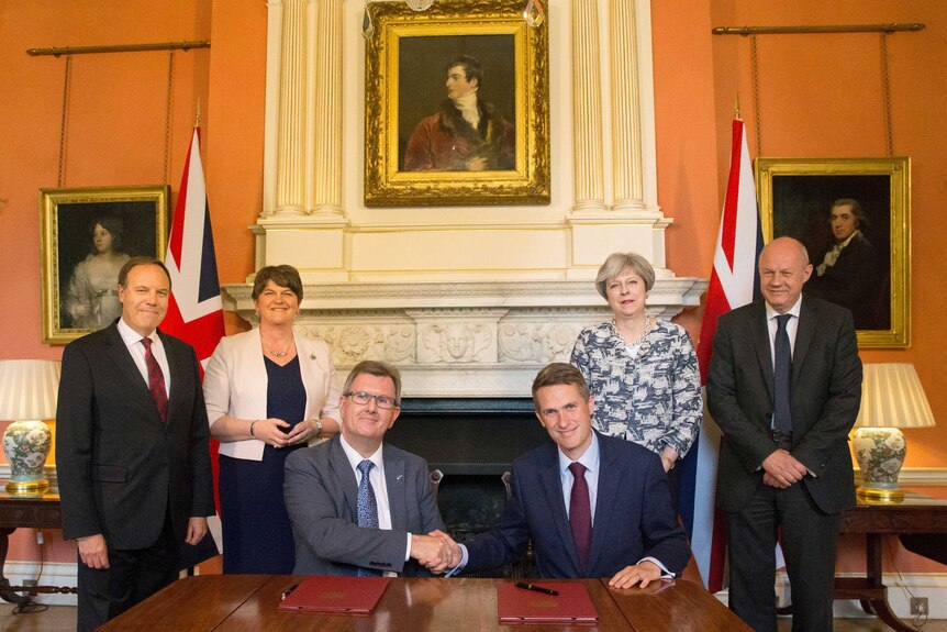 Jeffrey Donaldson and Gavin Williamson shake hands as Theresa May, Damian Green, Arlene Foster and Nigel Dodds stand behind.