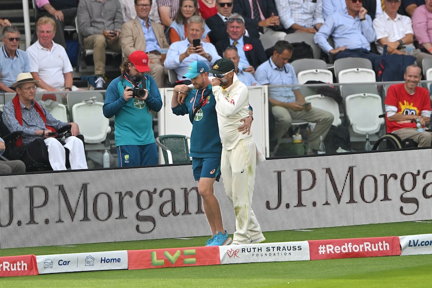 Nathan Lyon is helped around the boundary line by an Australian medico