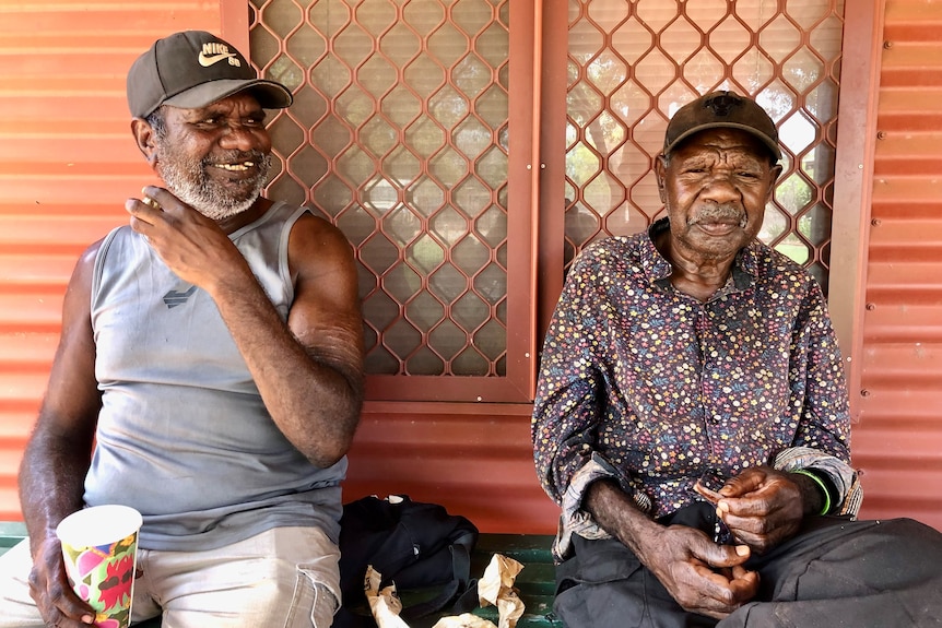 Two men sit smiling on a bench