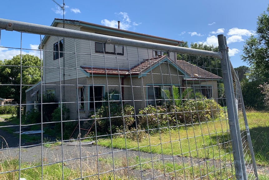 A wire fence around a two-storey house that been severely vandalised