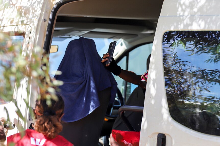 An young Aboriginal women's hand is visible through a van door holding a phone for a selfie 