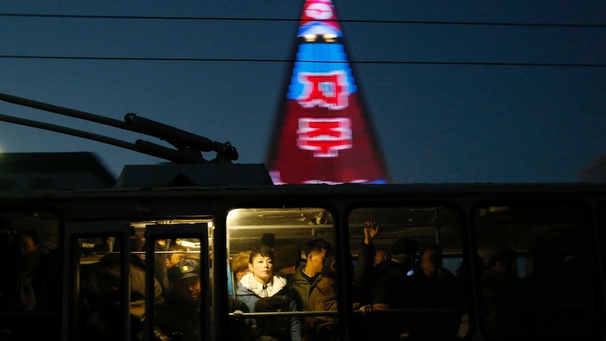 People ride on a tram as a propaganda message is partially seen displayed on the facade of the pyramid-shaped Ryugyong Hotel.