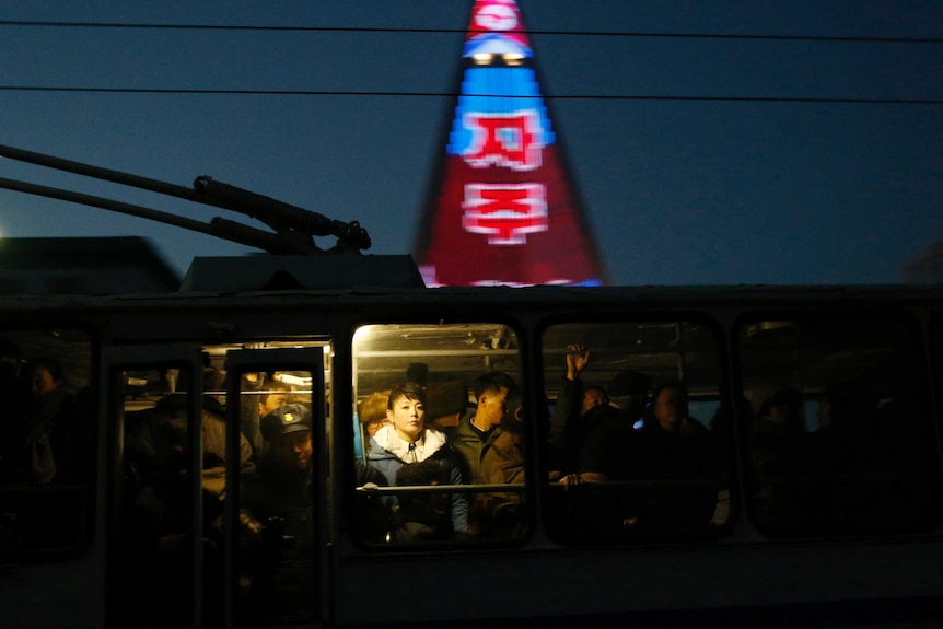 People ride on a tram as a propaganda message is partially seen displayed on the facade of the pyramid-shaped Ryugyong Hotel.