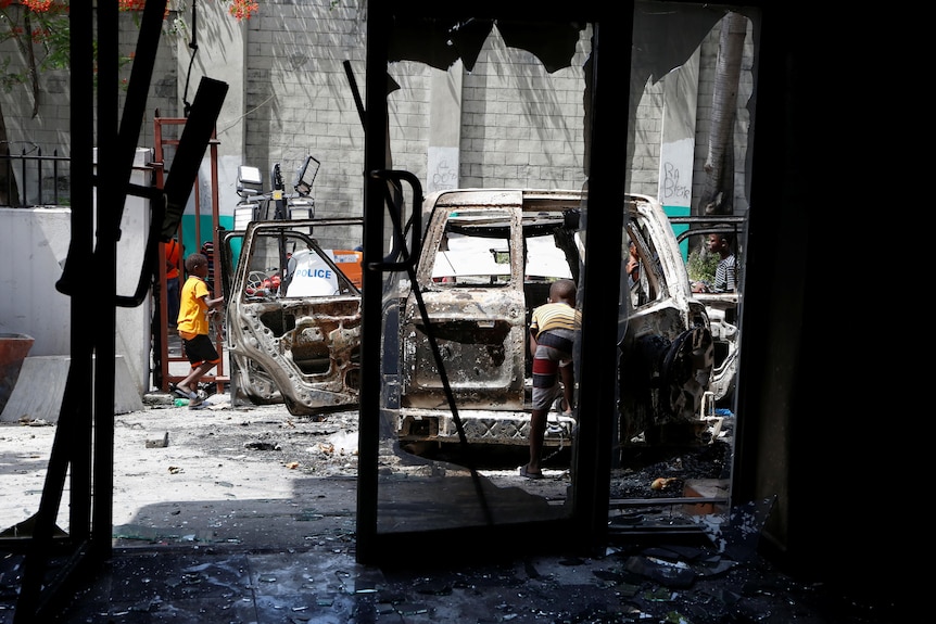 Children near a burned out car seen from the interior of a burned out building. 