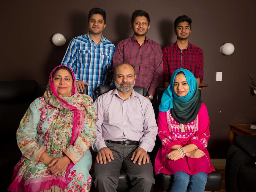 Umer, Danial and Ali stand in front of their mum, dad and sister who are sitting on chairs in their living room.