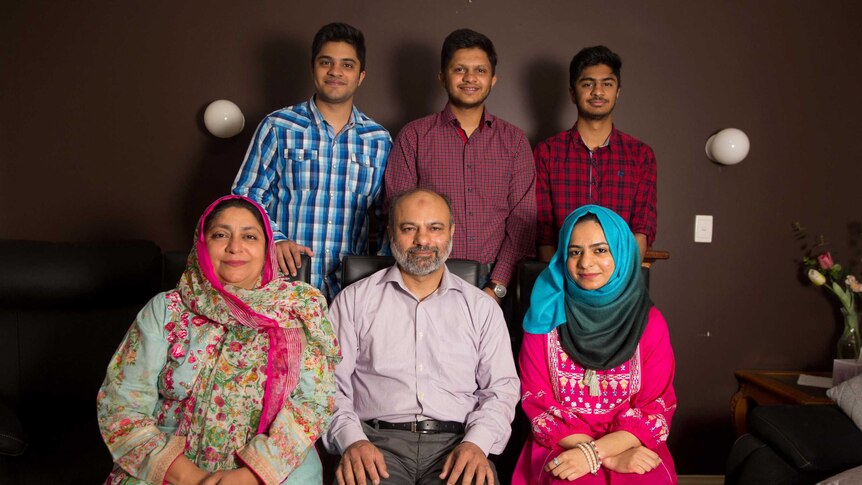 Umer, Danial and Ali stand in front of their mum, dad and sister who are sitting on chairs in their living room.