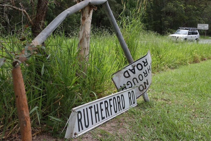 A broken sign saying Rutherford Road on grass.
