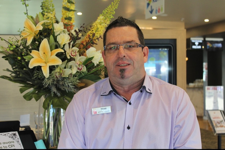 A man with short dark hair and a neat goatee stands in front of a flower display in a lobby.